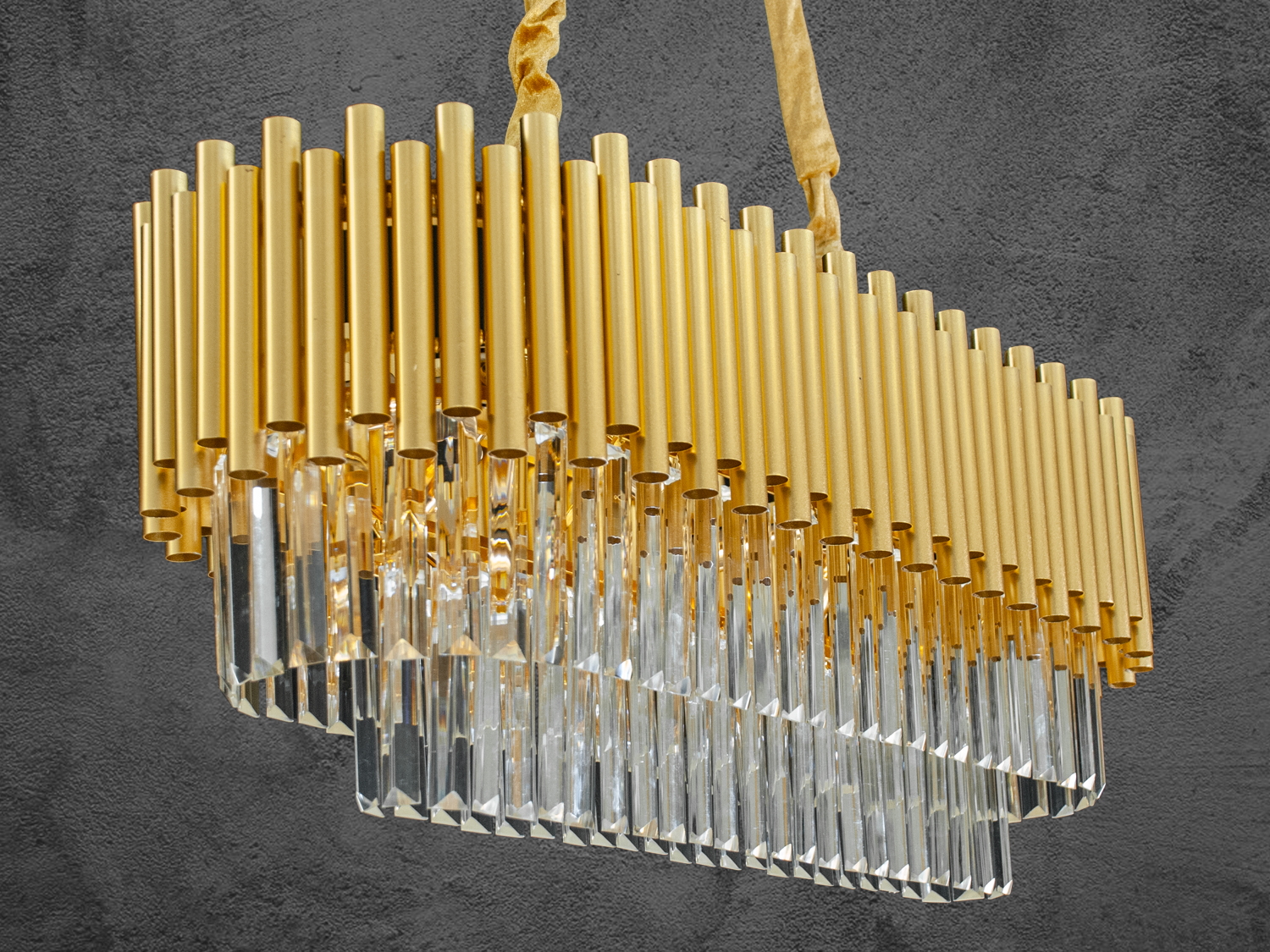 Демонструє всю красу люстри в підвішеному стані - витончені металеві трубки в золотистому кольорі і кришталеві підвіски, що переливаються.