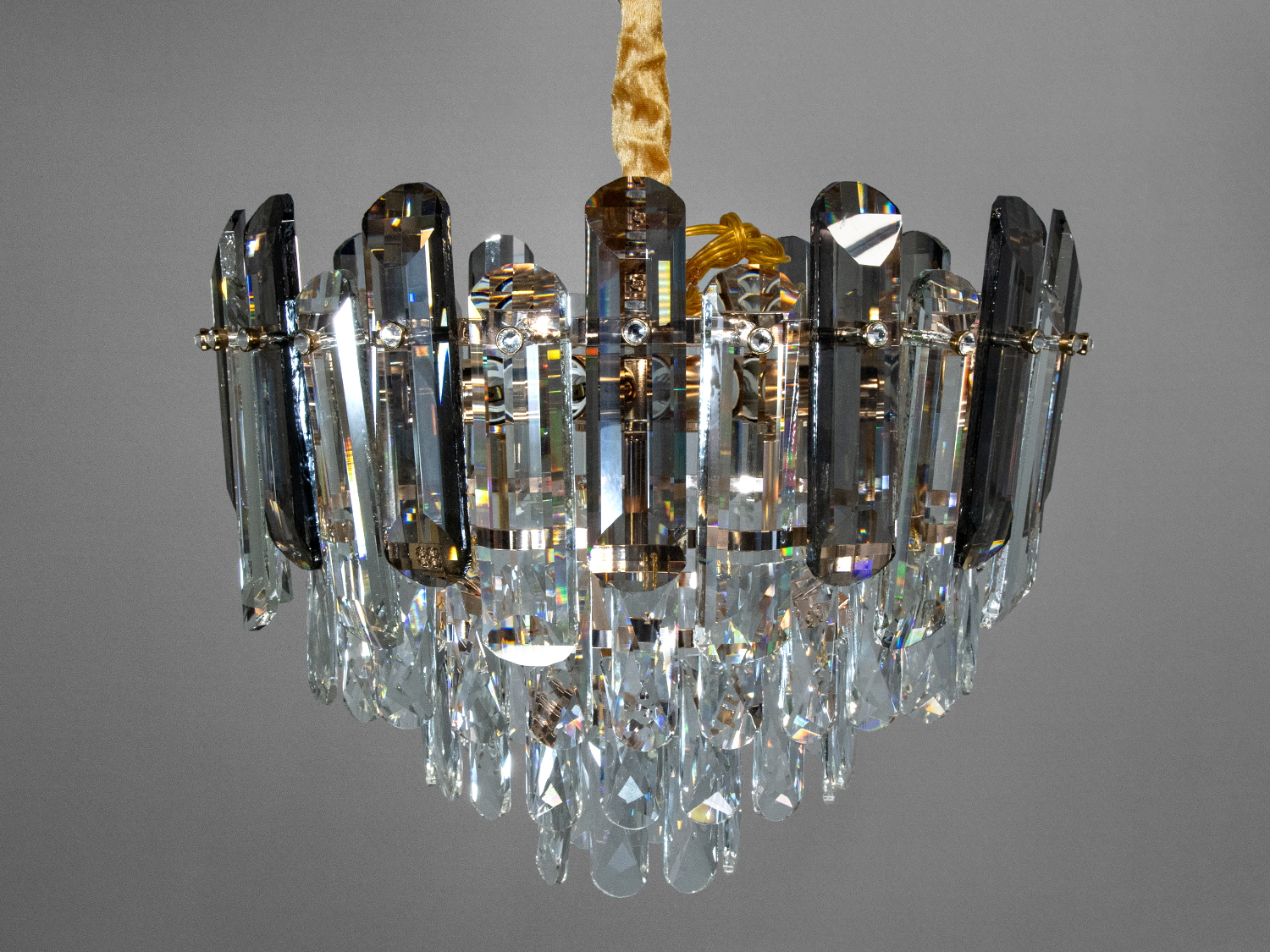 Люстра з кришталевими підвісками, підвісний монтаж, темні металеві елементи, відображає світло в різних кольорах.