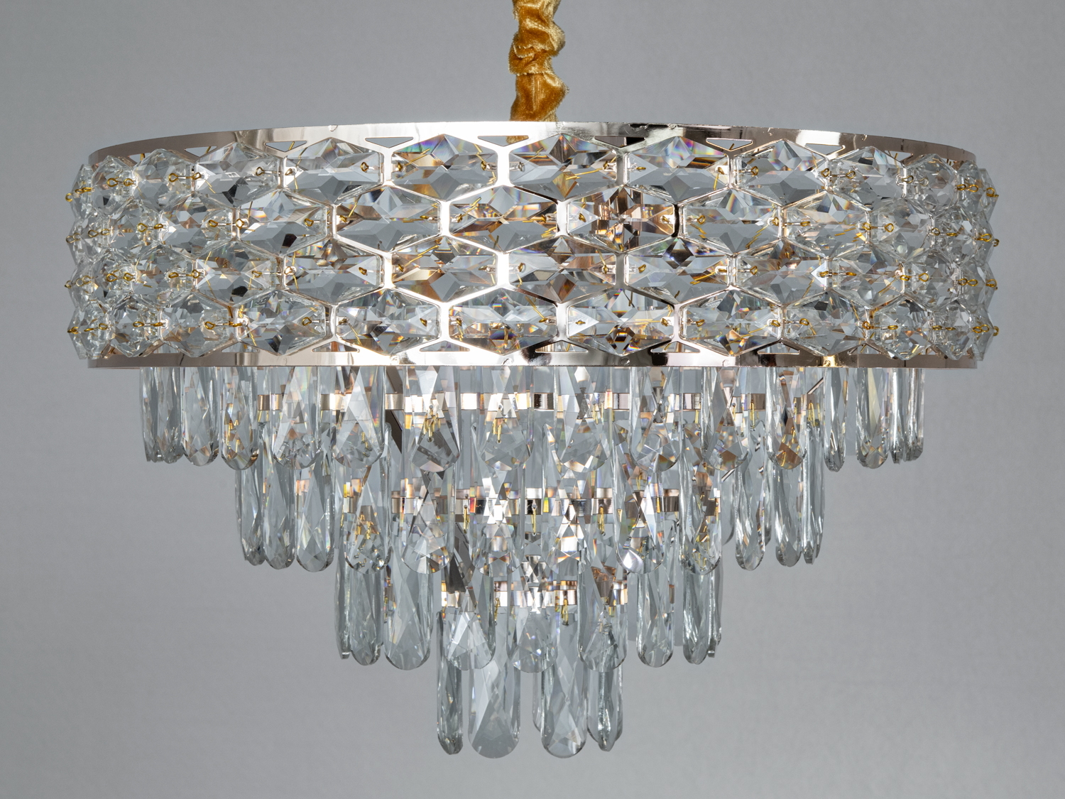 Люстра з багатоярусними кришталевими підвісками, встановлена на металевій основі, створює розкішний світловий ефект.