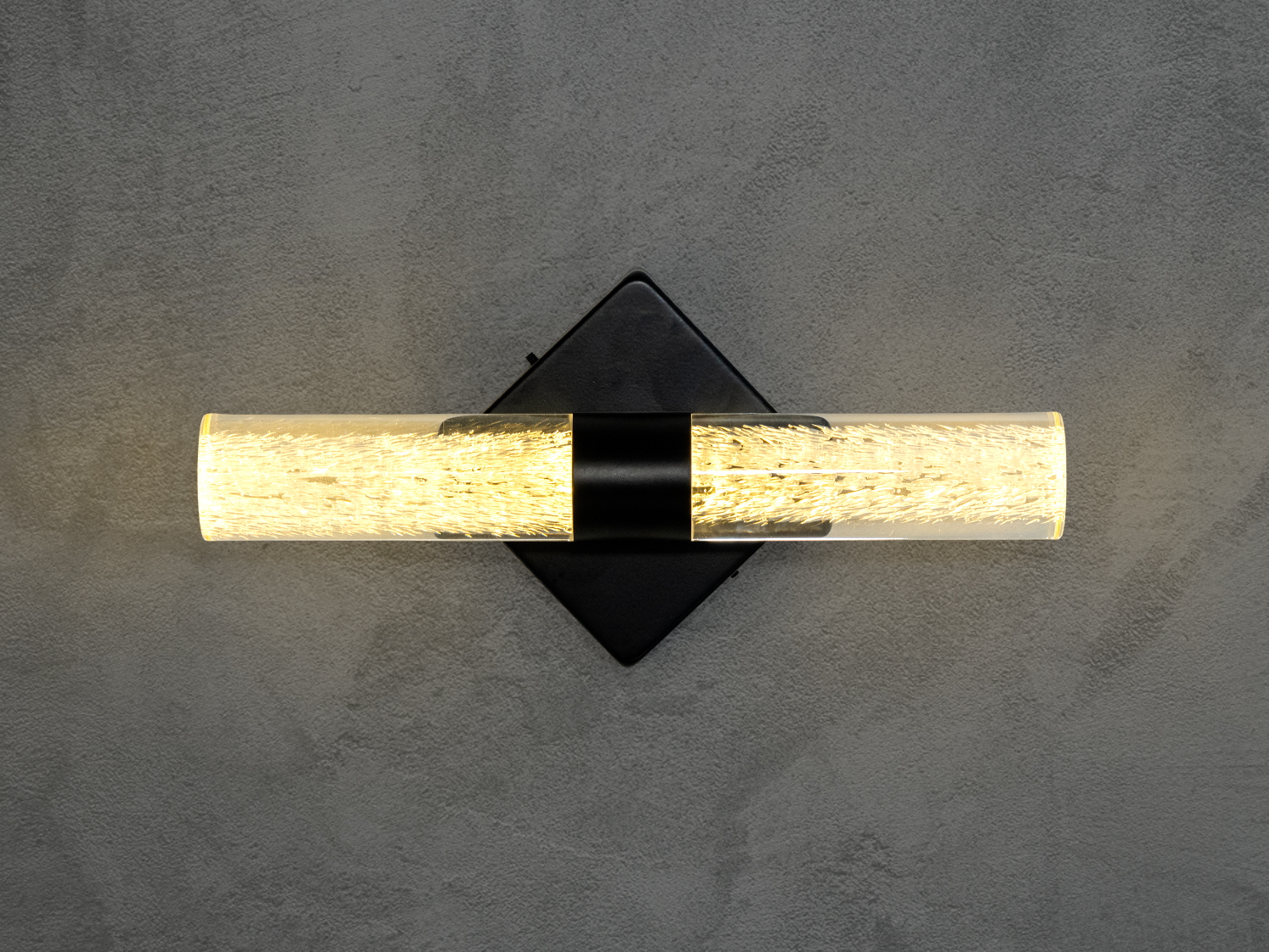 Настінний світильник із циліндричним скляним плафоном, що випромінює тепле світло. Підходить для сучасного інтер’єру.