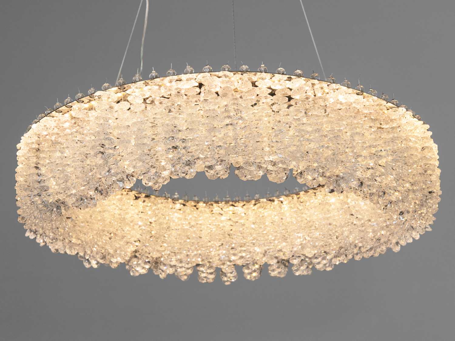 Люстра у формі кільця з кришталевими елементами, що підвішена на тросах. Підходить для вітальні, додає елегантності простору.