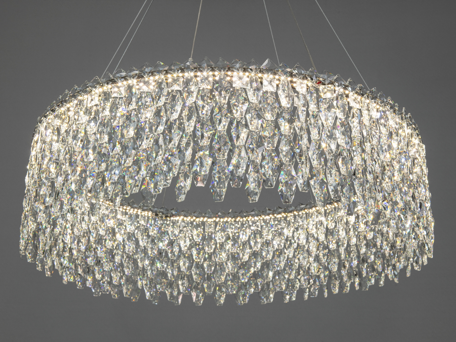 Кругла люстра з прозорими кришталевими елементами, що відбивають світло. Підходить для вітальні або їдальні, підвісна конструкція.