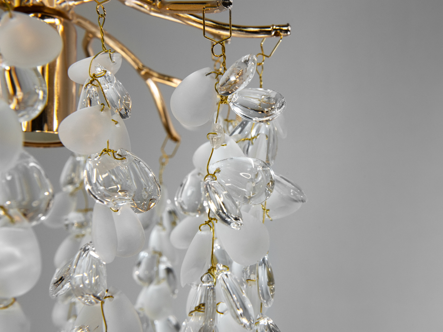 Деталі люстри з фокусом на матові та прозорі скляні підвіски, підвішені на золотистій арматурі, додають елегантності.