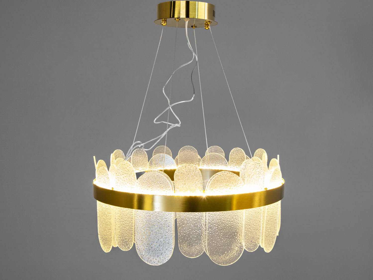 Люстра з прозорими скляними панелями, що створюють м’яке світло. Золотистий металевий обідок підкреслює сучасний стиль.