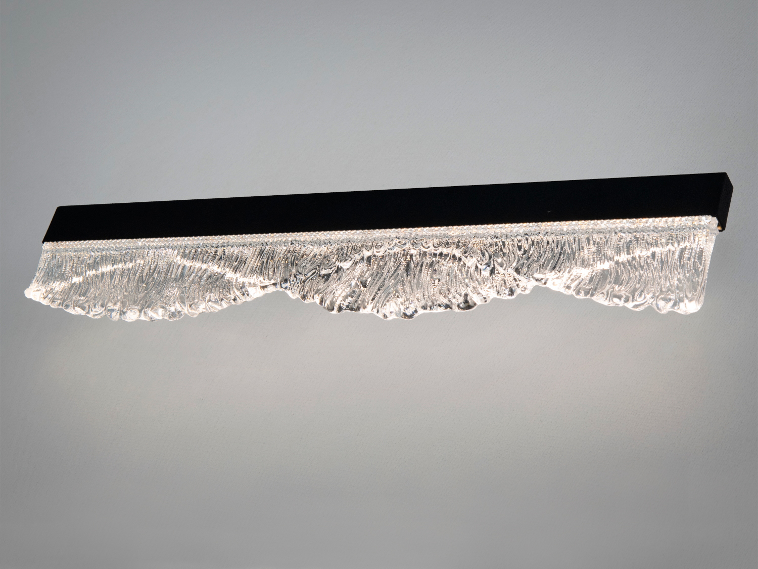 Світильник з чорним корпусом і хвилястим скляним елементом. Використовується для декоративного освітлення.