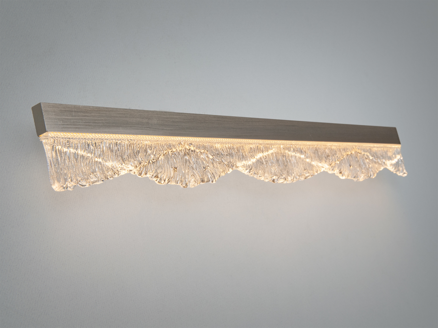 Настінний світильник з текстурованим скляним абажуром, що імітує хвилі, випромінює тепле світло, ідеальний для сучасних просторів.