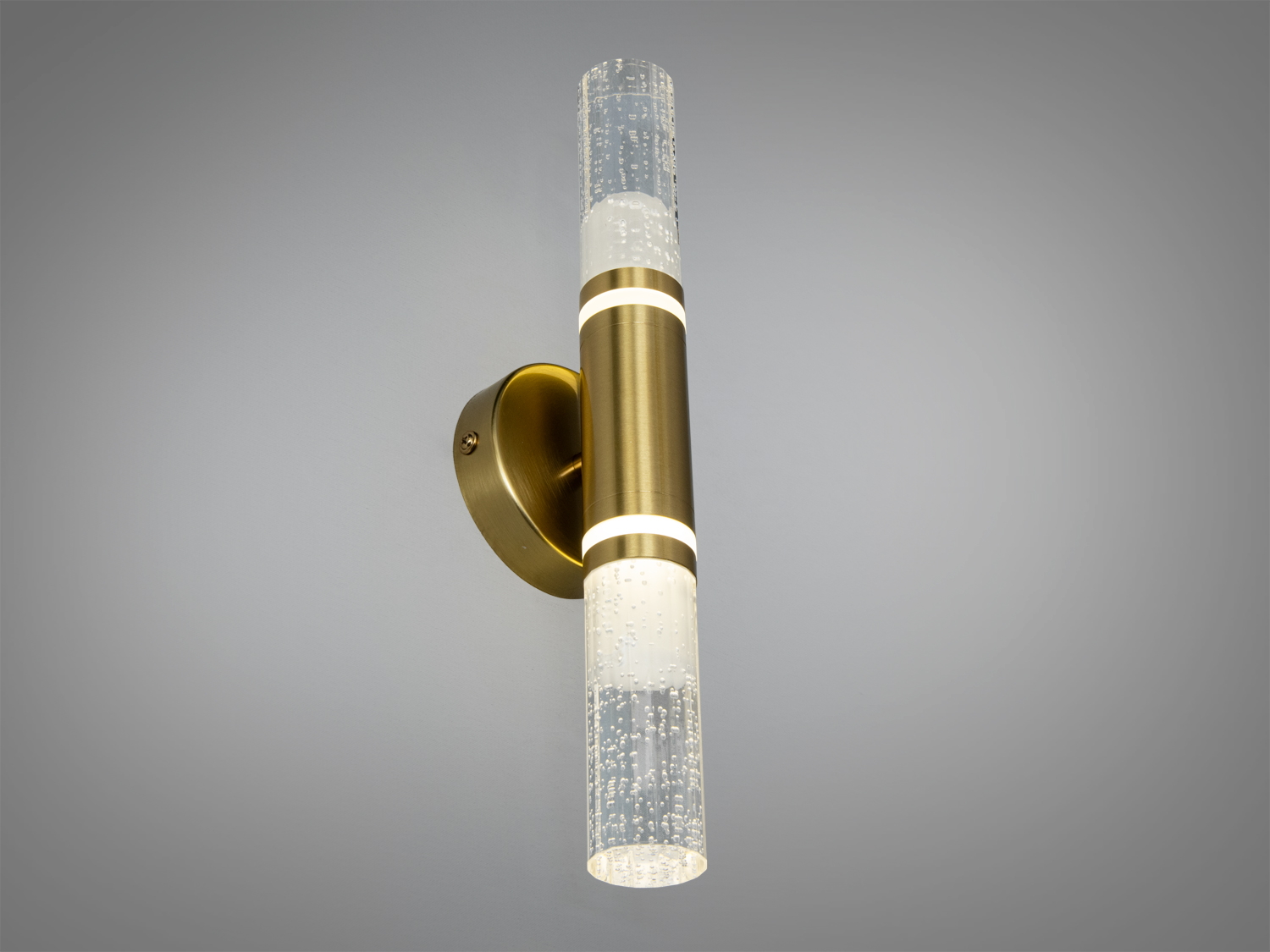 Настінний світильник з горизонтальним розташуванням, циліндричний плафон з прозорого скла з бульбашками, металеве кріплення золотого кольору.