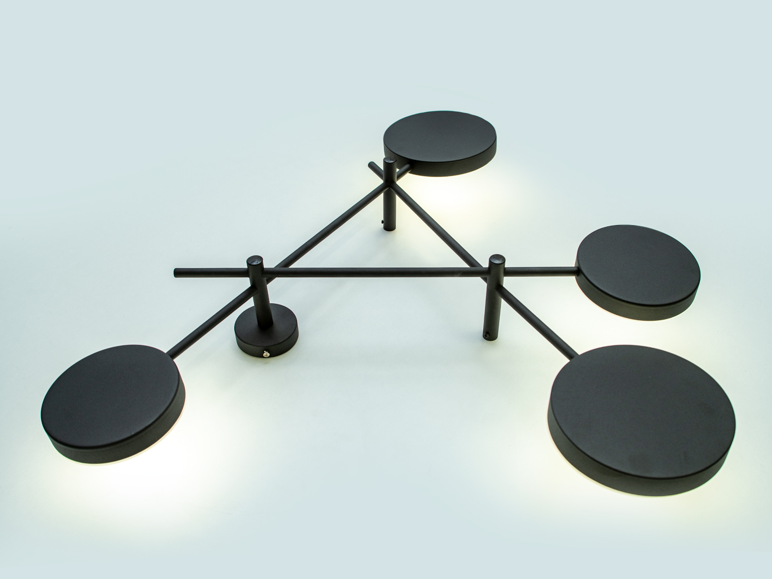Чорний настінний світильник з чотирма круглими елементами, що створюють геометричний візерунок. Виготовлений з металу.