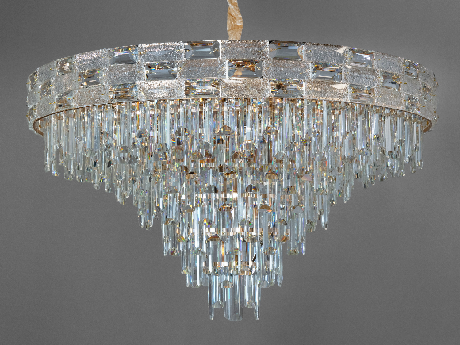 Ця чудова класична кришталева люстра стане окрасою будь-якого інтер′єру, додаючи йому нотки розкоші та елегантності. Виготовлена з якісних матеріалів, вона поєднує у собі блиск кришталю та шляхетність металу кольору хром, що робить її ідеальним вибором для створення розкішної атмосфери у вашому будинку.
Люстра складається з декількох ярусів підвісок з кришталю та скла, які чудово відбивають світло, створюючи гру світла та тіней на стінах та стелі. Дизайн доповнений оксамитовим чохлом, що надає моделі особливого шику та витонченості. Люстра підвішується на елегантному ланцюзі, висоту люстри можна регулювати від 65 до 100см, що дозволяє адаптувати освітлення під будь-які потреби та розміри приміщення.
Модель оснащена 19 лампами з цоколем E14, кожна з яких може бути потужністю до 40 Вт. Ви можете вибрати лампи розжарювання для більш теплого та затишного світла або світлодіодні лампи для більш ефективного та довговічного освітлення. Така гнучкість у виборі ламп забезпечує не лише гарне, а й практичне освітлення.
Ця кришталева люстра не просто освітлювальний прилад, а й приголомшлива прикраса, здатна змінити будь-який простір. Вона ідеально підійде для освітлення вітальні, їдальні або вестибюлю, додаючи кожному приміщенню вишуканості та урочистості.