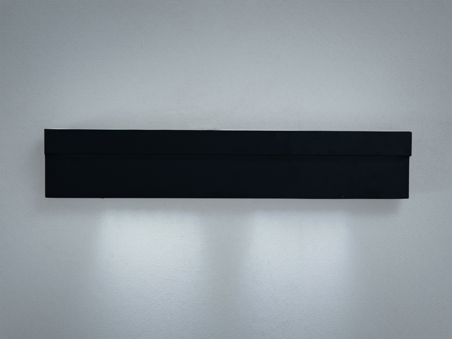 Настінний світильник чорного кольору з прямокутною формою, випромінює м′яке світло вниз. Підходить для сучасних інтер’єрів.