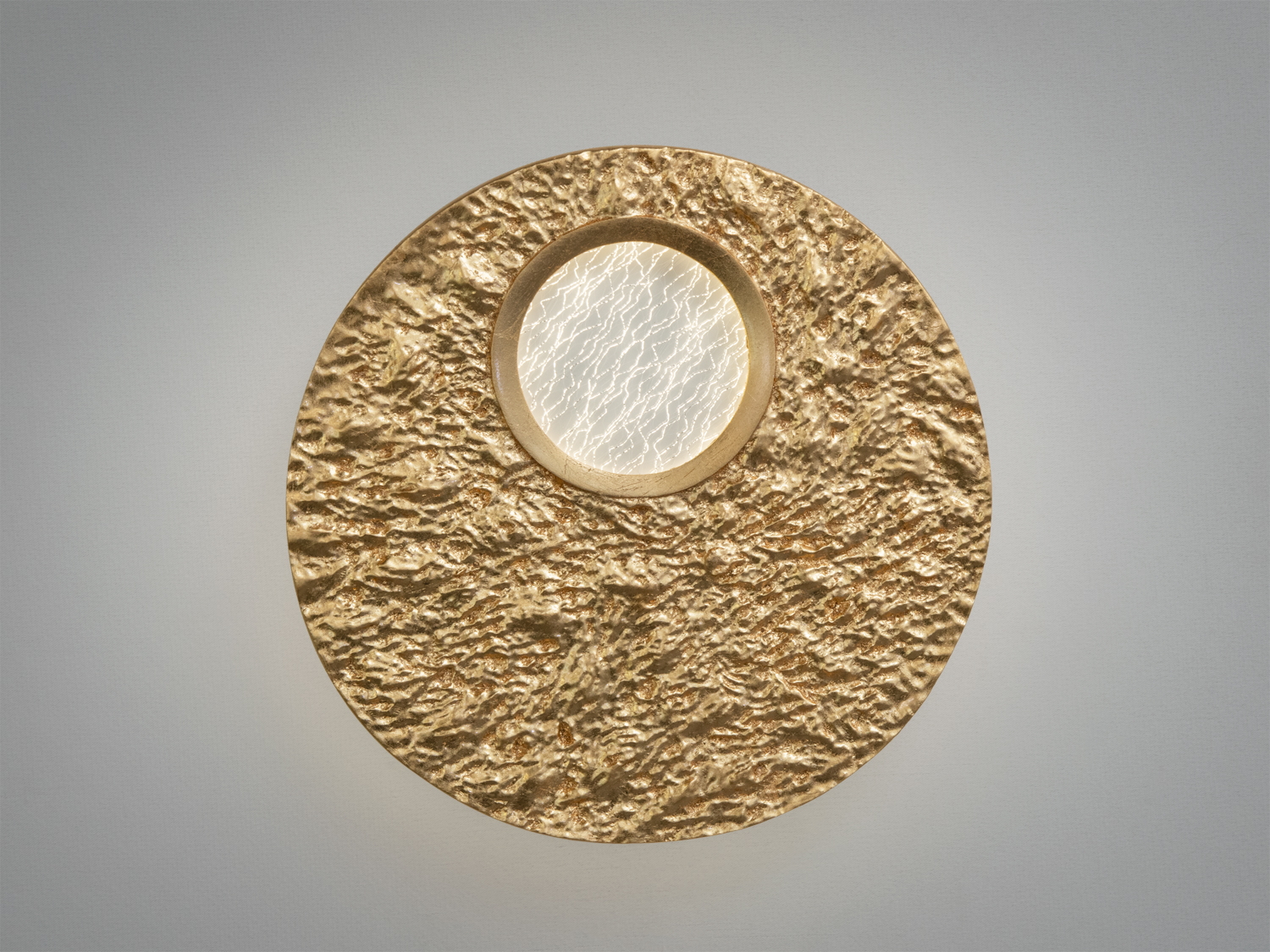 Настінний світильник круглої форми з текстурованою поверхнею. Центральна частина має прозоре скло з візерунком для розсіювання світла.