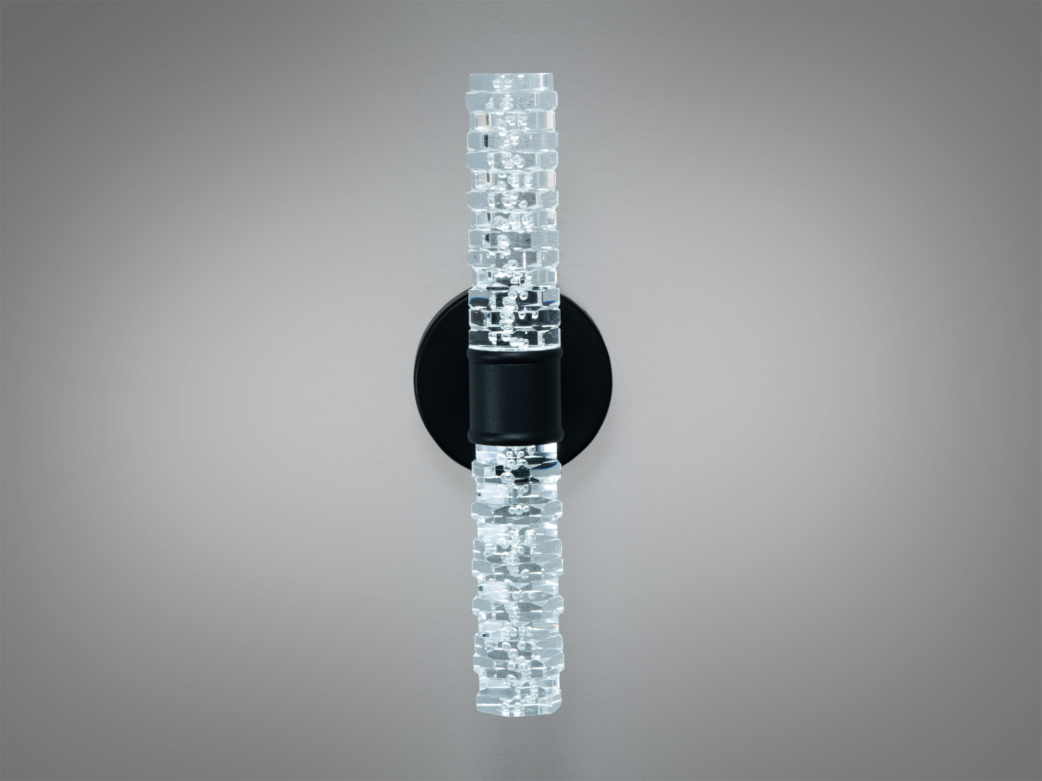 Настінний світильник з круглою чорною основою та прозорим трубчастим плафоном, що створює м’яке освітлення.