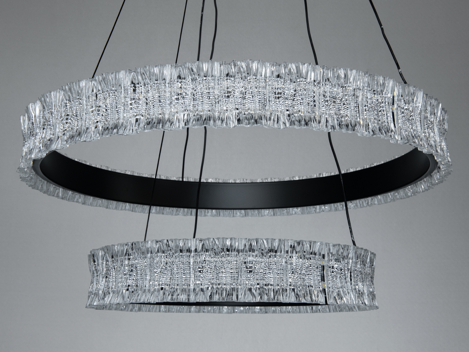 Два кільця підвісного світильника з кристалами, чорний металевий каркас. Підходить для вітальні або спальні, створює елегантну атмосферу.