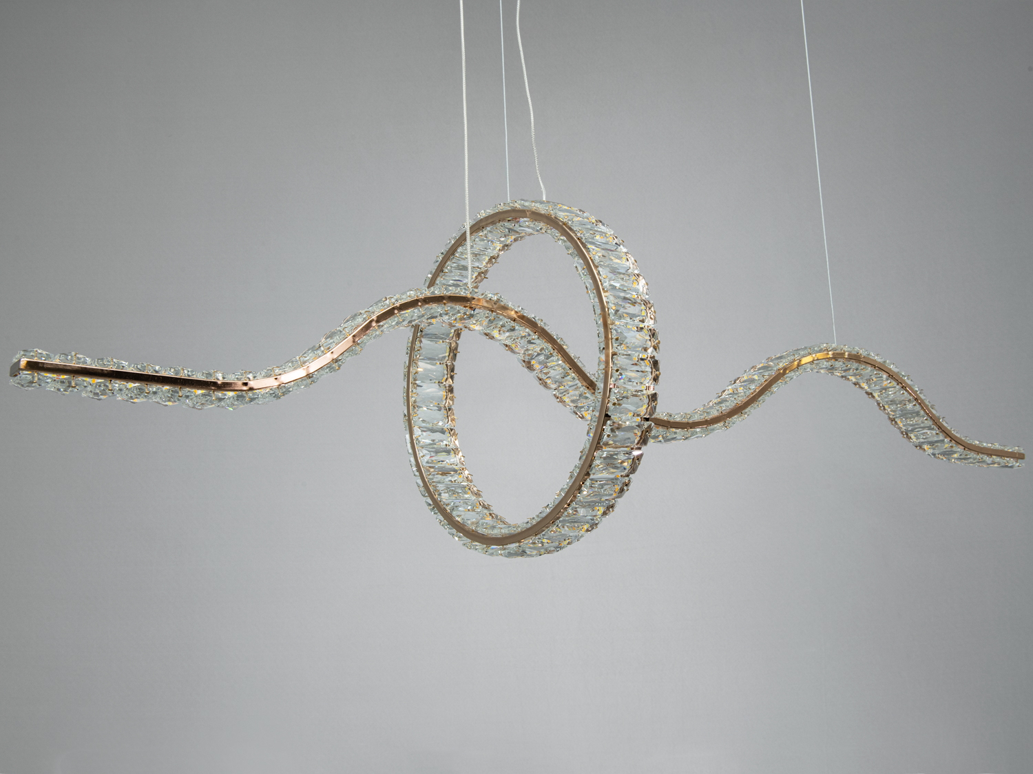 Кришталевий світильник з хвилястими лініями, підвішений на тонких тросах. Ідеальний для освітлення вітальні.