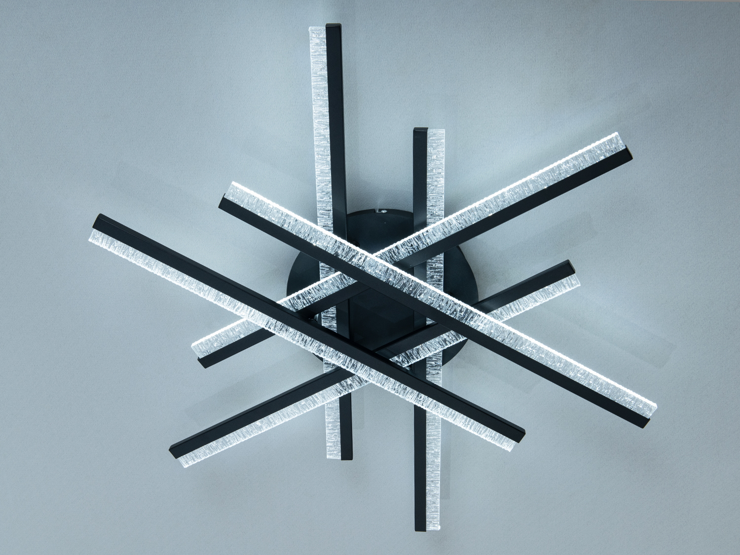 Настінний світильник з чорними планками, що перетинаються, і прозорими краями. Випромінює холодне біле світло, підходить для офісу.