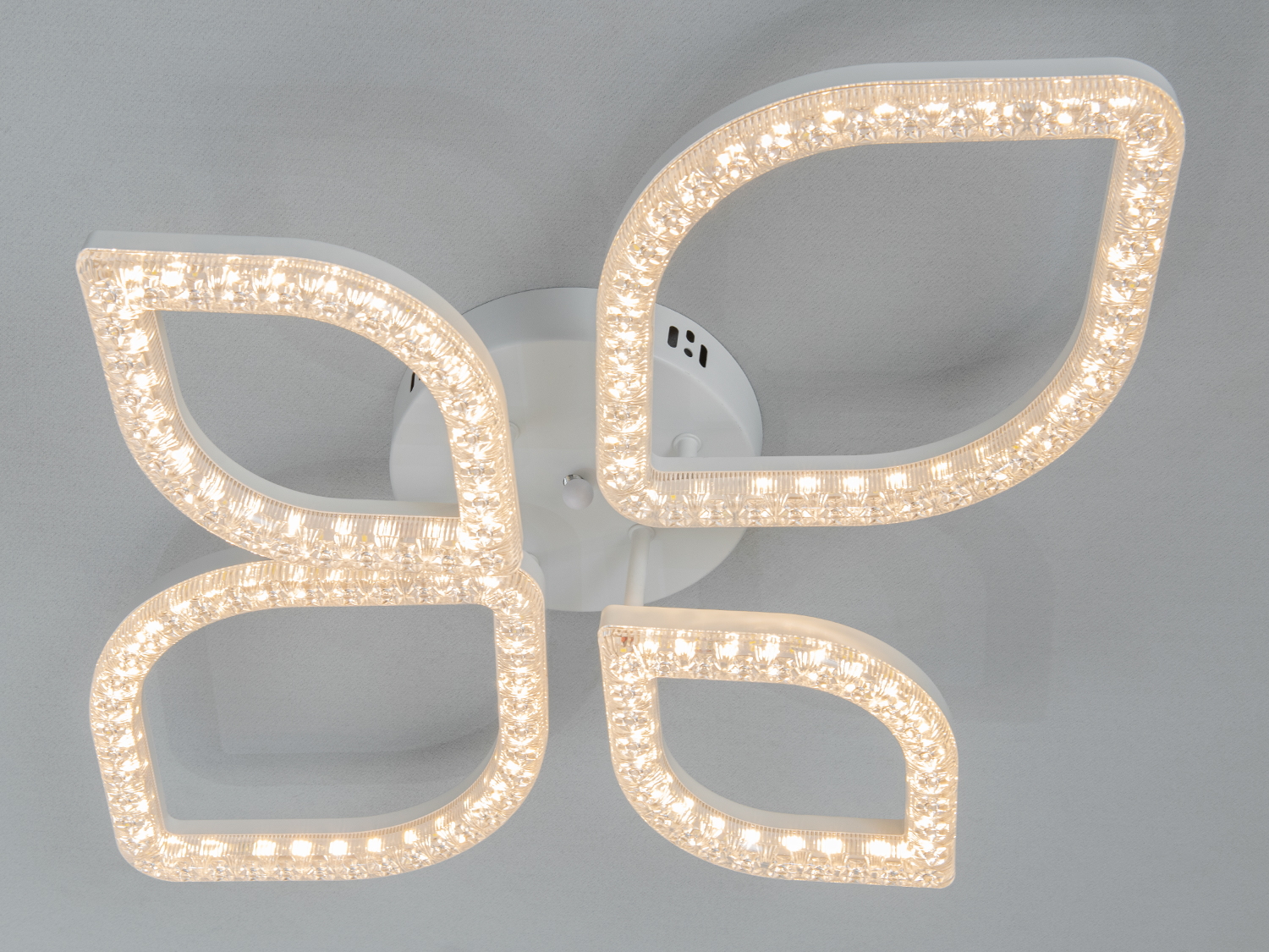 Стельовий світильник з теплим світлом, має чотири елементи у формі пелюсток, ідеально підходить для вітальні.