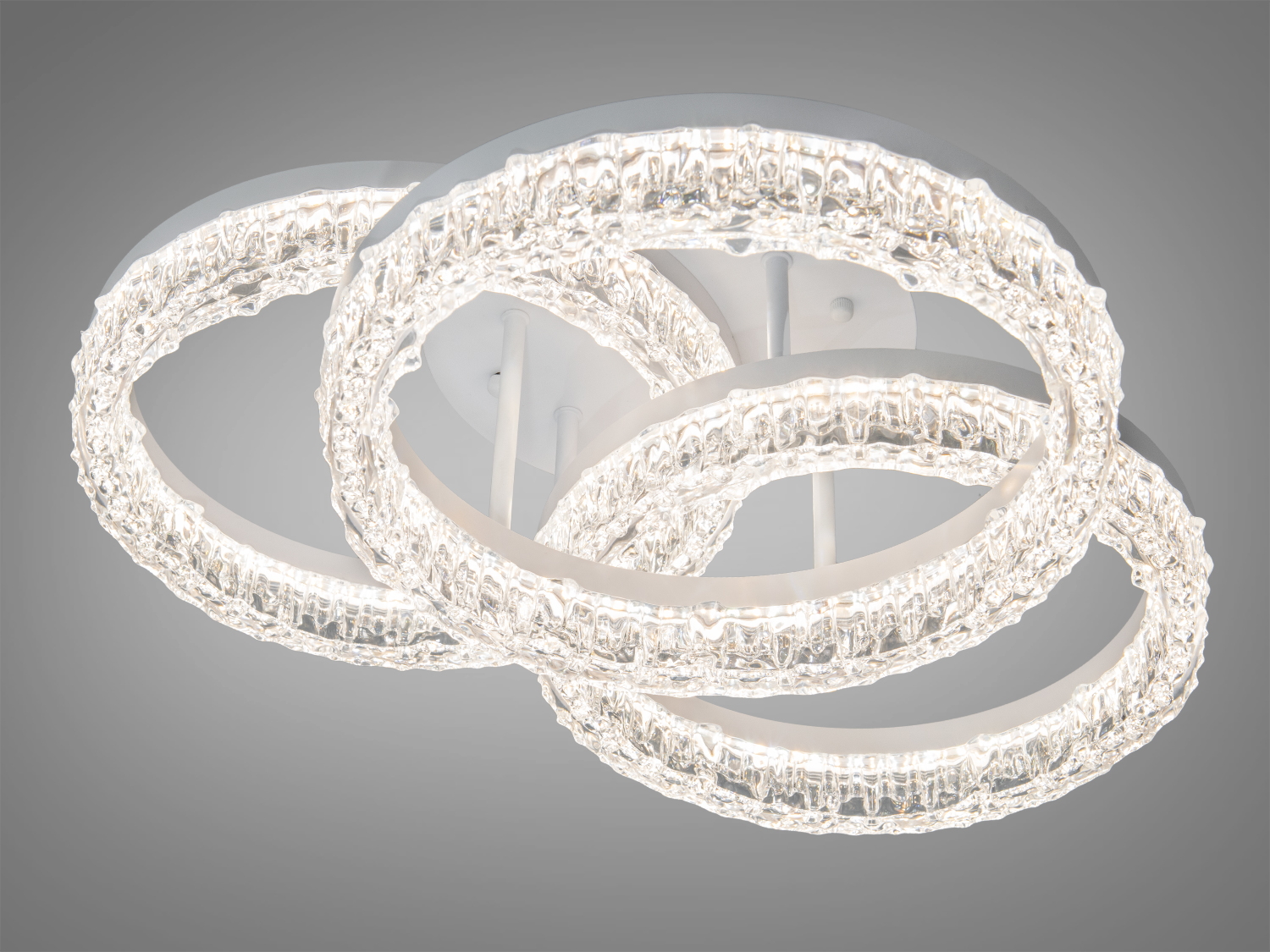 Стельова люстра з трьома прозорими кільцями, що перетинаються, створює м’яке освітлення для вітальні.