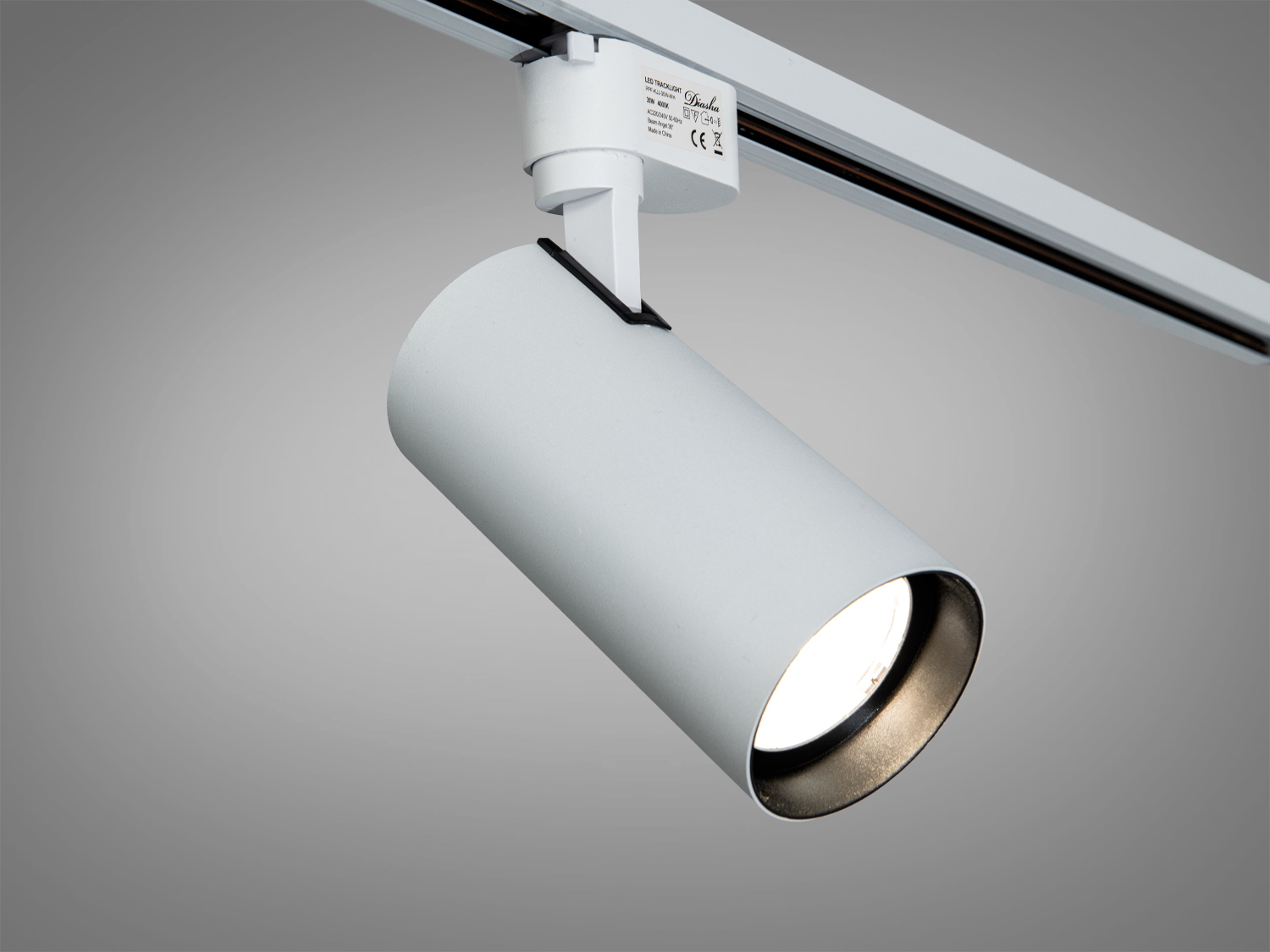 Білий циліндричний трековий світильник з LED-лампою, підвішений на рейці. Призначений для акцентного освітлення в інтер′єрі.