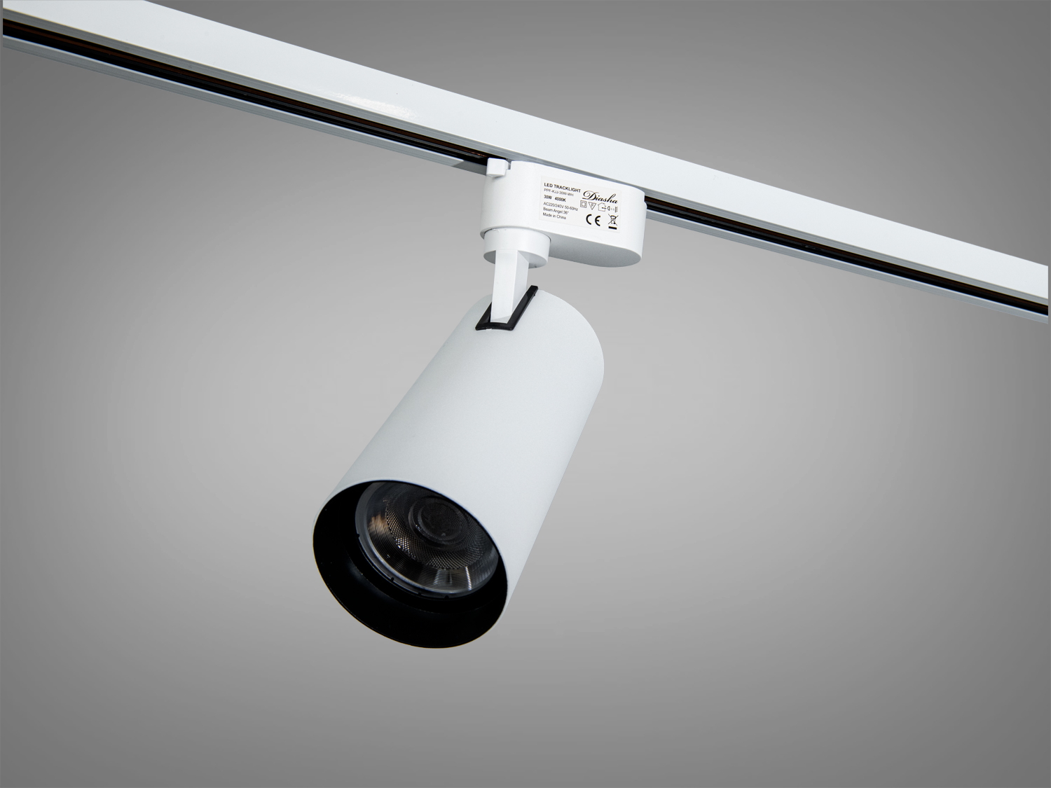 Трековий світильник циліндричної форми з білим корпусом, закріплений на треку. Використовується для спрямованого освітлення.