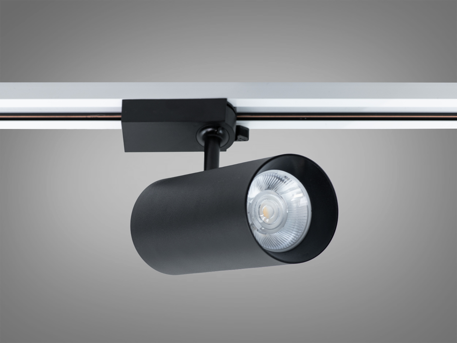 Трековий світильник з чорним циліндричним корпусом, оснащений лінзою для фокусування світла, ідеальний для галерей.