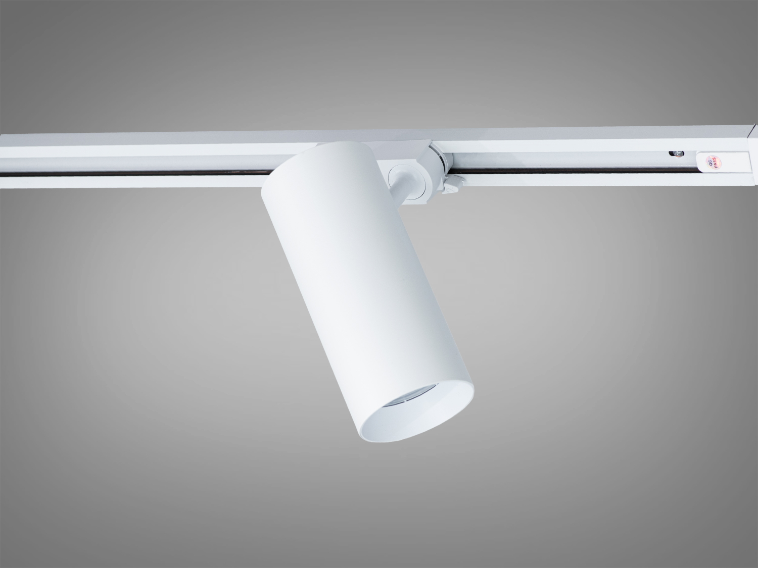 Білий циліндричний світильник на треку, нахилений під кутом для регулювання напрямку світла в приміщенні.