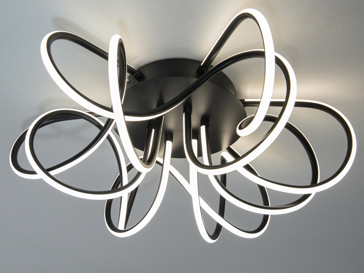 Сучасний світильник з чорним металевим корпусом і вигнутими світлодіодними елементами, що підходить для монтажу на стелі у просторих кімнатах.