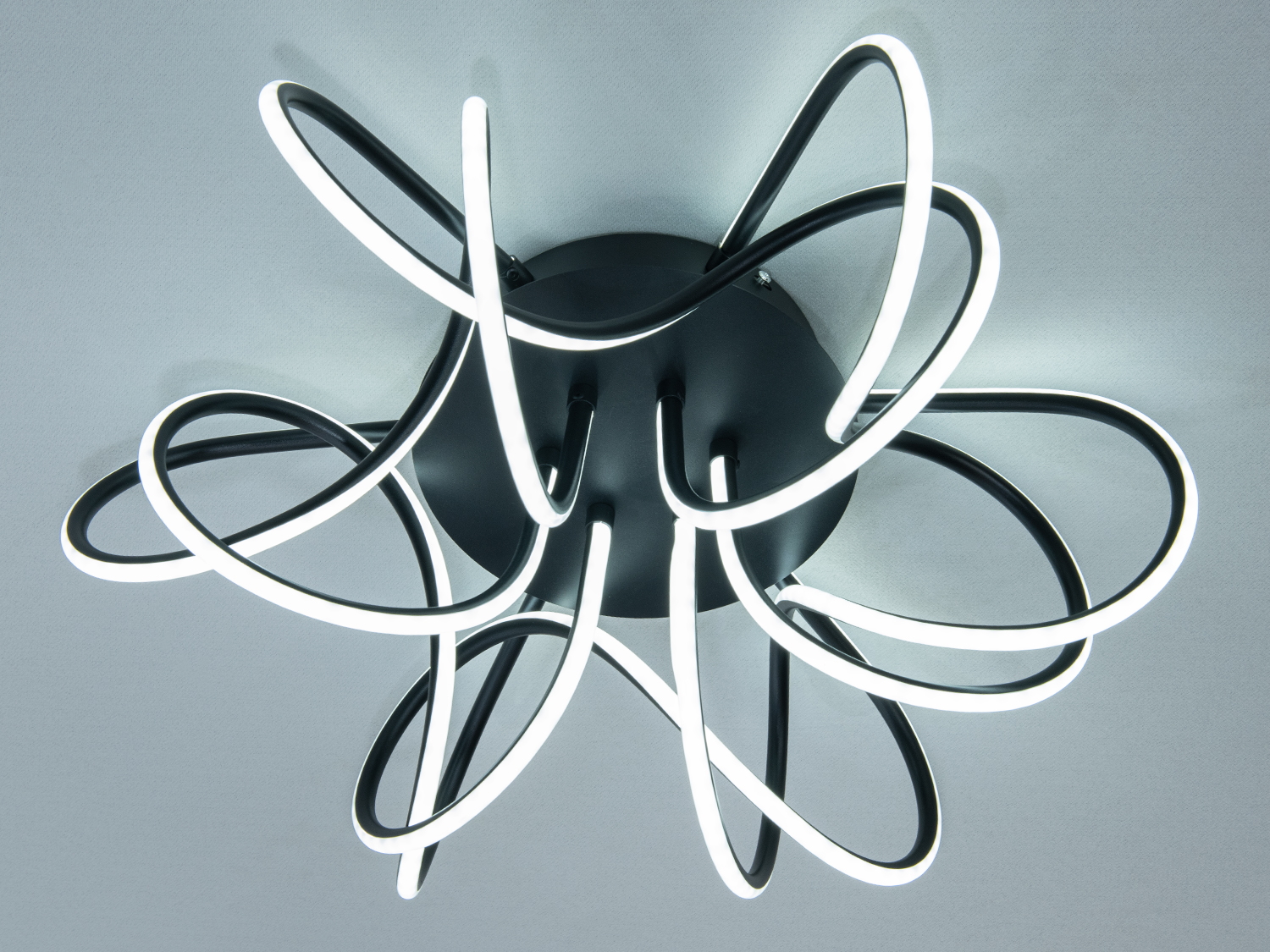 Дизайнерський світильник з чорним металевим корпусом і вигнутими світлодіодними трубками, що забезпечують м’яке освітлення в сучасному інтер’єрі.